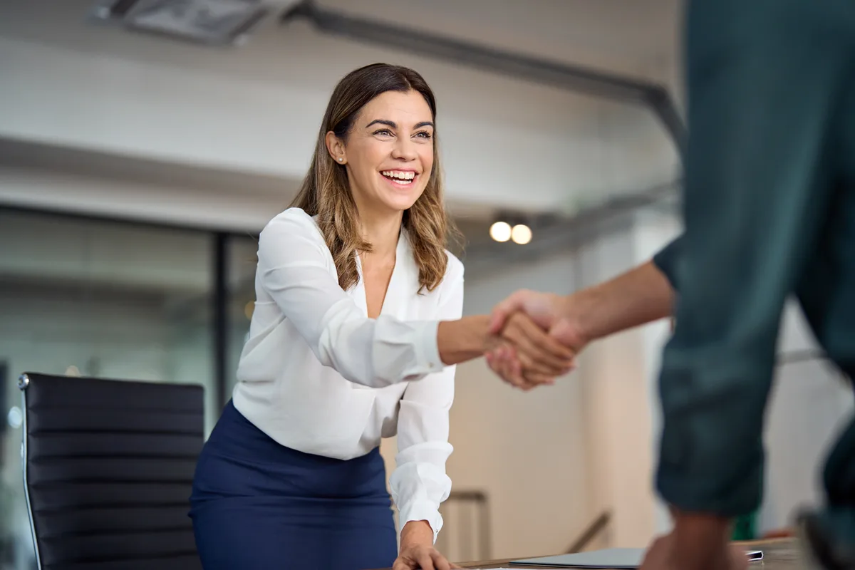 Business owner and buyer shaking hands across a table after signing a share purchase agreement