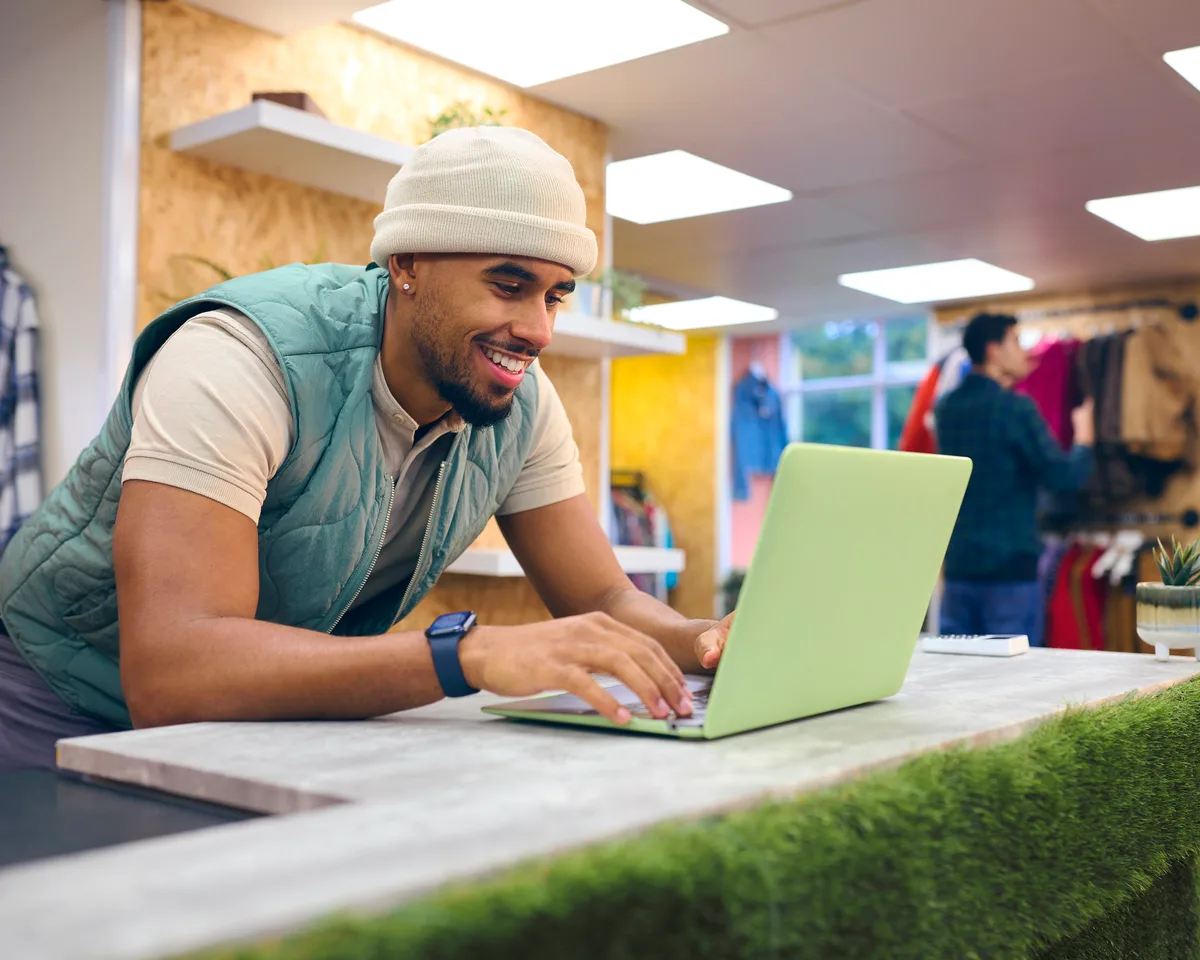 Laptop on a small business desk showing a cloud accounting dashboard with a receipt scanner app on a phone beside it
