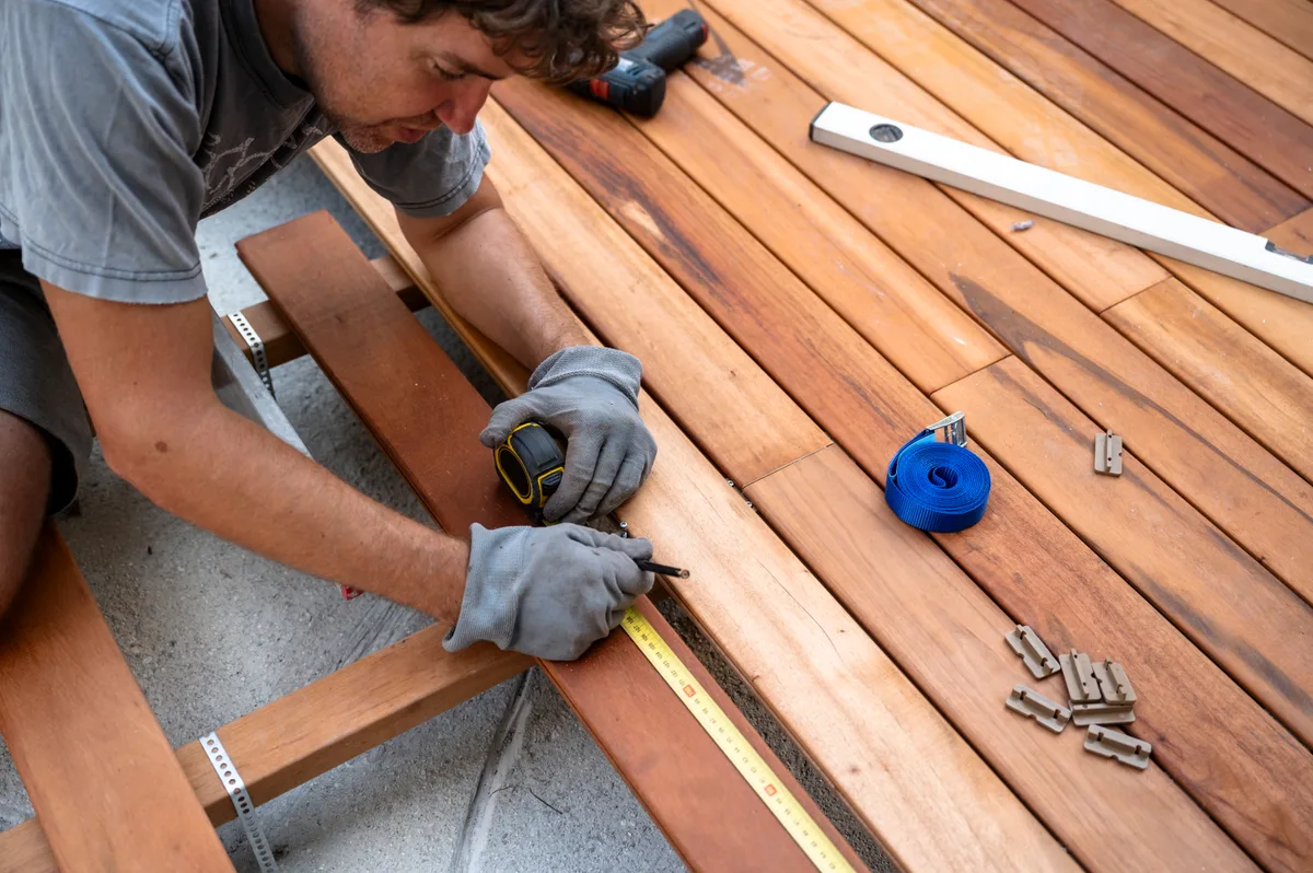 Deck builder measuring and cutting lumber on a residential job site