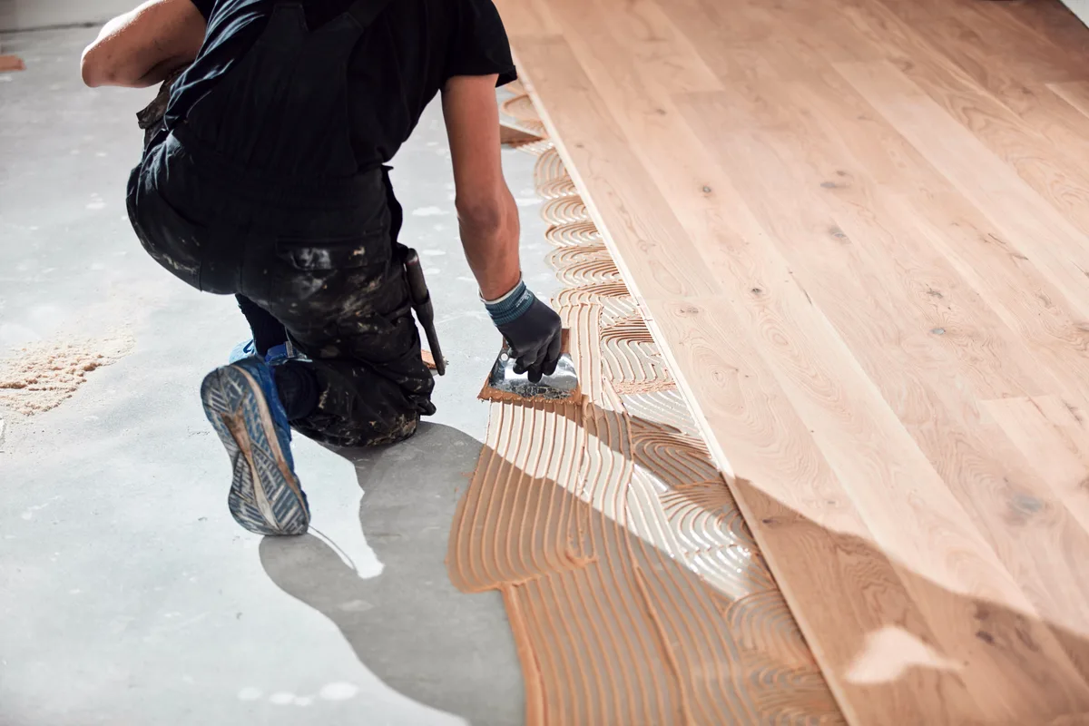 Flooring installer laying hardwood planks in a residential room