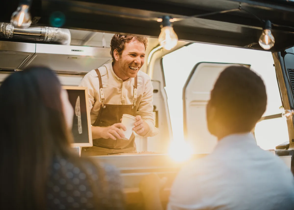Customers ordering at the window of a food truck parked on a city street