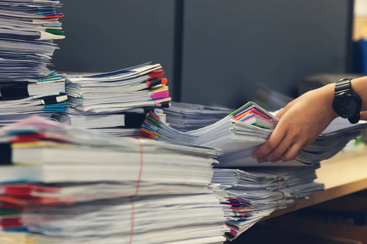 Desk covered in unsorted receipts and bank statements beside a laptop showing an accounting ledger