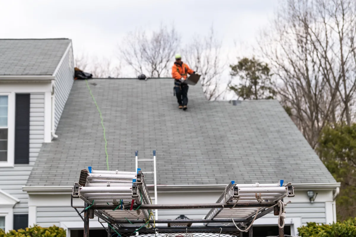 Roofer installing asphalt shingles on a steep residential roof