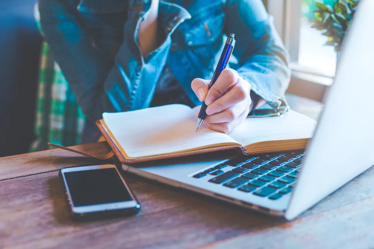 Author writing on a laptop beside stacks of books